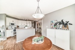 Open-concept kitchen and dining area featuring white cabinetry, light countertops, wood-finish flooring, and a contemporary pendant light fixture - 