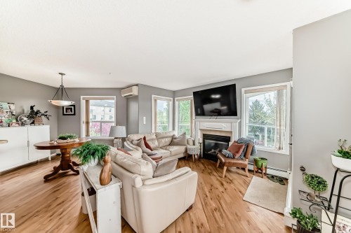 Living area featuring wood-finish flooring, a fireplace with a white mantel, and multiple windows - 331 9704 174 Street, Edmonton, AB - Indoor Photo Showing Living Room With Fireplace