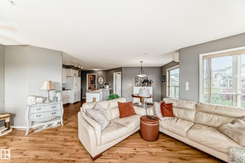 Open-concept living area with wood-finish flooring, ample natural light from large windows, and a kitchen featuring white cabinetry and appliances - 331 9704 174 Street, Edmonton, AB - Indoor Photo Showing Living Room