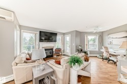 Living area featuring wood-finish flooring, a white fireplace with mantle, multiple windows, and a glass-paneled exterior door - 