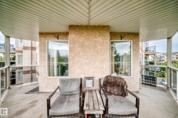 Spacious balcony featuring a textured stucco exterior, white-framed windows, a slatted ceiling, and glass panel railings - 