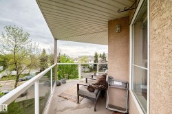 Private balcony featuring a textured stucco exterior, white soffit, and clear glass panel railings - 