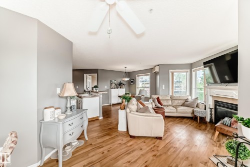 Open-concept living space with wood-finish flooring, a white fireplace surround, and multiple windows - 331 9704 174 Street, Edmonton, AB - Indoor Photo Showing Living Room With Fireplace