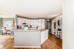 Open-concept kitchen featuring white cabinetry, light countertops, and wood-finish flooring - 