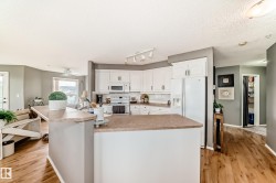Spacious kitchen featuring white cabinetry, light countertops, wood-finish flooring, and a full suite of white appliances - 