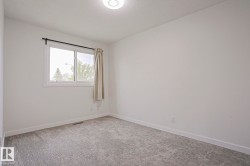 Bright room featuring a window with white trim, light gray patterned carpeting, white baseboards, and a flush-mount ceiling light fixture - 