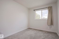 Bright interior room featuring a large window, light gray patterned carpeting, white baseboards, and white walls - 