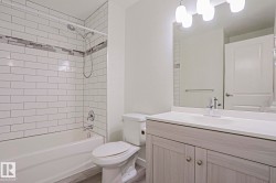 Bathroom featuring a tub/shower combination with white subway tile surround and decorative accent band, a single vanity with wood-finish cabinetry, a light-toned countertop, and a large wall mirror - 