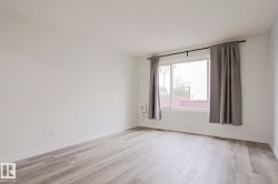 Spacious room featuring light wood-finish flooring, white baseboards, and a large window with grey drapes - 