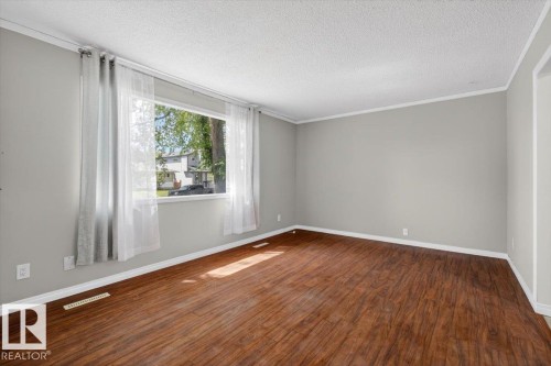 Spacious room featuring wood-finish flooring, a large window, light gray wall paint, white baseboards, and a white ceiling - 4630 114 Avenue, Edmonton, AB - Indoor Photo Showing Other Room