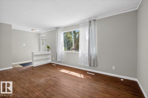 Open-concept living space with wood-finish flooring, a large window, light gray walls, white trim, and a built-in half-wall bookshelf - 4630 114 Avenue, Edmonton, AB - Indoor Photo Showing Other Room