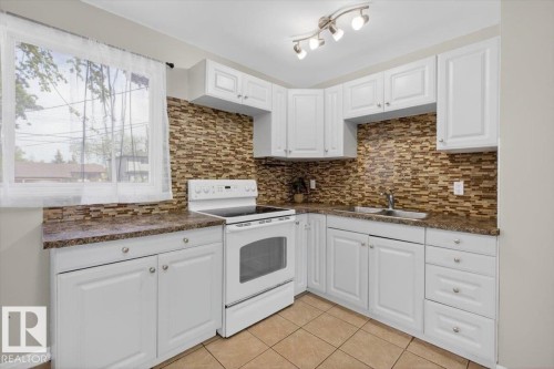 Kitchen featuring white cabinetry, a white electric range, a stainless steel sink, and a multi-toned tile backsplash - 4630 114 Avenue, Edmonton, AB - Indoor Photo Showing Kitchen With Double Sink