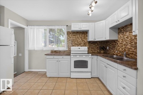 Kitchen featuring white cabinetry with brushed nickel hardware, a mosaic tile backsplash, and speckled countertops - 4630 114 Avenue, Edmonton, AB - Indoor Photo Showing Kitchen With Double Sink
