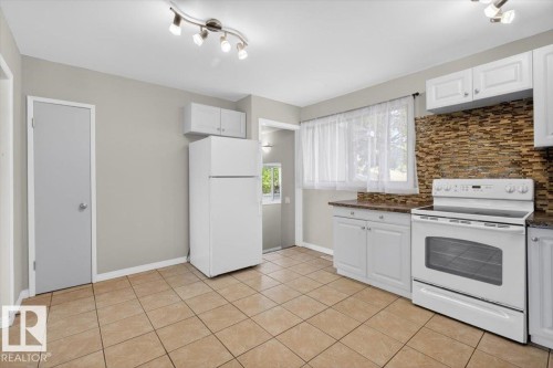 Kitchen featuring tile flooring, white cabinetry, a white electric range, and a textured stone backsplash - 4630 114 Avenue, Edmonton, AB - Indoor Photo Showing Kitchen
