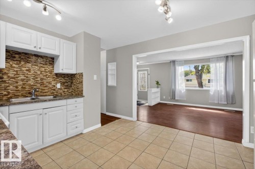 Kitchen area featuring white cabinetry, a brown mosaic tile backsplash, and a sink with a chrome faucet - 4630 114 Avenue, Edmonton, AB - Indoor Photo Showing Kitchen With Double Sink