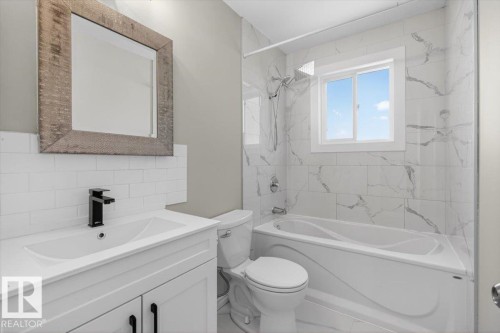 Bathroom featuring a white vanity with matte black hardware and faucet, a rectangular mirror with a textured frame, white subway tile backsplash, and a white bathtub with a shower - 4630 114 Avenue, Edmonton, AB - Indoor Photo Showing Bathroom