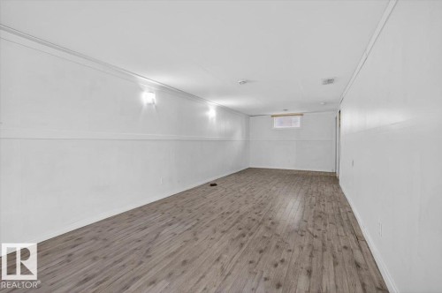 Spacious room featuring wood-finish flooring, white walls, recessed ceiling lights, and two wall-mounted sconces - 4630 114 Avenue, Edmonton, AB - Indoor Photo Showing Other Room