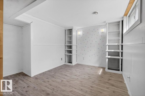 Room featuring wood-finish flooring, two built-in shelving units, wall-mounted sconces, and a window - 4630 114 Avenue, Edmonton, AB - Indoor Photo Showing Other Room