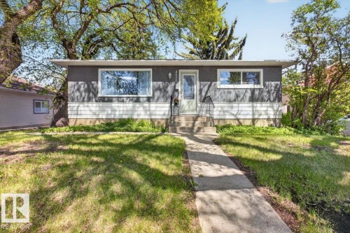 Front exterior featuring a gray stucco finish with white horizontal siding accent, a white entry door with frosted glass, and white-framed windows - 4630 114 Avenue, Edmonton, AB - Outdoor