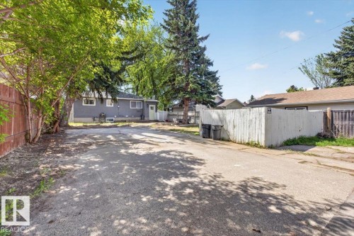 Paved rear yard with fencing, mature trees, and a gray exterior home with white trim windows - 4630 114 Avenue, Edmonton, AB - Outdoor