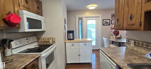 Kitchen featuring wood-finish cabinetry, patterned tile backsplash, solid surface countertops, and white appliances - 5113 45 B Avenue, Vegreville, AB - Indoor Photo Showing Kitchen