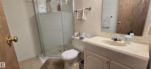 Bathroom featuring a glass-enclosed shower, white toilet, single vanity with integrated sink, and wood-finish door - 5113 45 B Avenue, Vegreville, AB - Indoor Photo Showing Bathroom