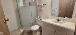 Bathroom featuring a glass-enclosed shower, white toilet, single vanity with integrated sink, and wood-finish door - 