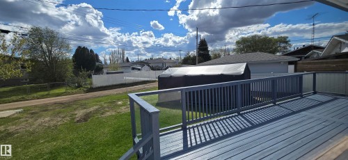 Spacious outdoor deck featuring gray wood-finish decking and railings with integrated opaque paneling, overlooking a large grass yard - 5113 45 B Avenue, Vegreville, AB - Outdoor