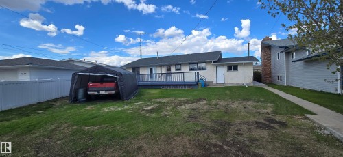 Rear exterior featuring a spacious wooden deck with a dark railing, a stucco finish on the main structure, and a dark shingle roof - 5113 45 B Avenue, Vegreville, AB - Outdoor With Deck Patio Veranda