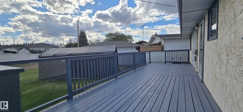 Expansive wooden deck with gray finish, featuring a surrounding railing, direct access to the interior, and an adjacent green space - 5113 45 B Avenue, Vegreville, AB - Outdoor