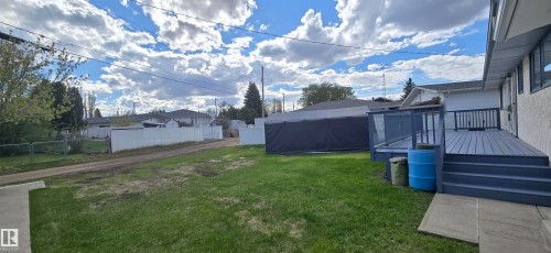 Expansive green lawn with a large, multi-level wooden deck featuring a grey finish and glass panel railings - 5113 45 B Avenue, Vegreville, AB - Outdoor