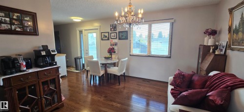 Dining area featuring a crystal chandelier, wood-finish flooring, a patio door with exterior access, and a large window with blinds - 5113 45 B Avenue, Vegreville, AB - Indoor Photo Showing Dining Room