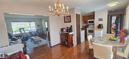 Hardwood-style flooring throughout the main living areas, featuring a dining space with a classic chandelier, and an open concept to a living room with an expansive window and outdoor decking - 5113 45 B Avenue, Vegreville, AB - Indoor Photo Showing Dining Room