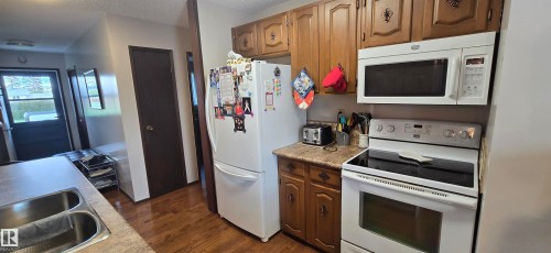 Kitchen featuring wood-finish flooring, wood cabinetry with decorative hardware, and white appliances including a range and over-the-range microwave - 5113 45 B Avenue, Vegreville, AB - Indoor Photo Showing Kitchen With Double Sink