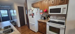 Kitchen featuring wood-finish flooring, wood cabinetry with decorative hardware, and white appliances including a range and over-the-range microwave - 