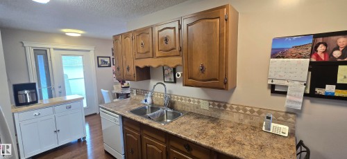 Kitchen featuring wood-finish cabinetry, a double basin stainless steel sink, and a patterned tile backsplash - 5113 45 B Avenue, Vegreville, AB - Indoor Photo Showing Kitchen With Double Sink