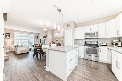 Open-concept living space featuring a contemporary kitchen with white cabinetry, stainless steel appliances, and a central island with a light-toned countertop - 2125 24 Street, Edmonton, AB - Indoor Photo Showing Kitchen With Stainless Steel Kitchen With Upgraded Kitchen