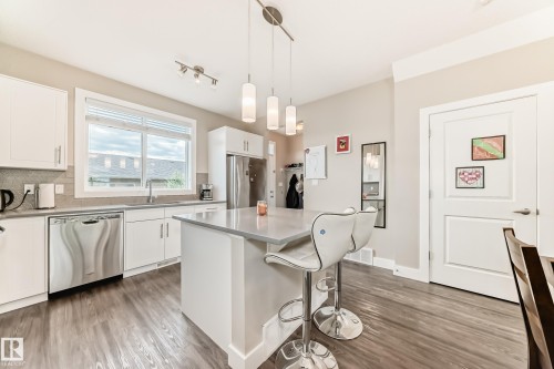 Modern kitchen featuring wood-finish flooring, white cabinetry, stainless steel appliances, and a central island with pendant lighting - 2125 24 Street, Edmonton, AB - Indoor Photo Showing Kitchen