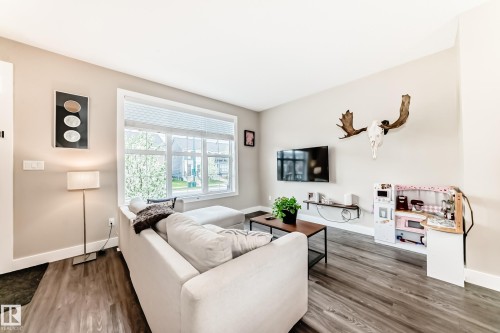 Bright living area featuring wood-finish flooring, neutral-toned walls, and a large window with white blinds - 2125 24 Street, Edmonton, AB - Indoor Photo Showing Living Room