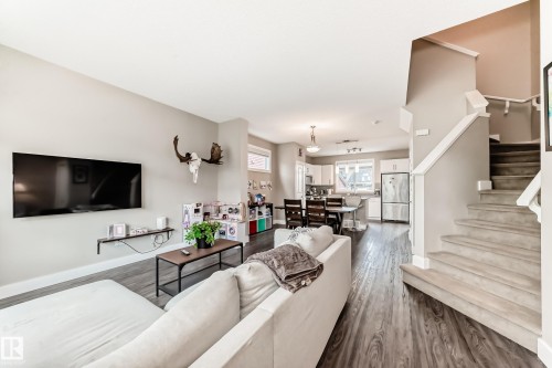 Open-concept living area featuring wood-finish flooring, a contemporary staircase with carpeted treads, and a kitchen with white cabinetry and stainless steel appliances - 2125 24 Street, Edmonton, AB - Indoor Photo Showing Living Room