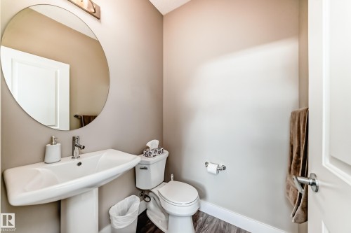 Powder room featuring a pedestal sink with chrome faucet, circular wall mirror, and wood-finish flooring - 2125 24 Street, Edmonton, AB - Indoor Photo Showing Bathroom