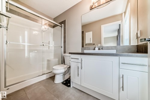 Bathroom featuring a full vanity with an integrated vessel sink, a large mirror, a shower with sliding glass doors, and tile flooring - 2125 24 Street, Edmonton, AB - Indoor Photo Showing Bathroom
