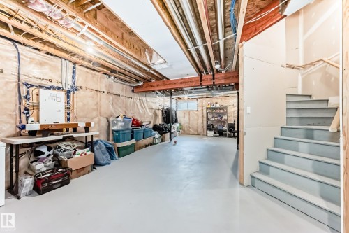 Unfinished basement space featuring exposed joists and insulation, a light-toned concrete floor, and a staircase with light blue treads - 2125 24 Street, Edmonton, AB - Indoor Photo Showing Basement