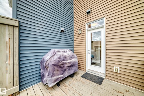 Private outdoor deck featuring wood planking, a full-lite exterior door with transom window, and exterior wall lighting - 2125 24 Street, Edmonton, AB - Outdoor With Deck Patio Veranda
