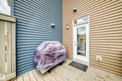 Private outdoor deck featuring wood planking, a full-lite exterior door with transom window, and exterior wall lighting - 
