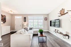 Spacious living area featuring wood-finish flooring, light neutral wall tones, and a large window with blinds - 