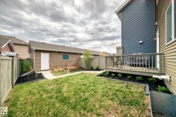 Spacious backyard featuring a wooden deck, a detached garage with exterior lighting, and a paved walkway - 