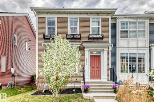 Two-story townhouse with beige horizontal siding and a salmon-colored front door - 2125 24 Street, Edmonton, AB - Outdoor With Facade