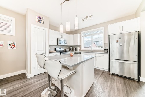 Modern kitchen featuring white cabinetry, stainless steel appliances, a center island with pendant lighting, a tile backsplash, and wood-finish flooring - 2125 24 Street, Edmonton, AB - Indoor Photo Showing Kitchen With Stainless Steel Kitchen