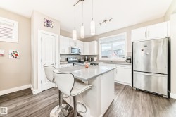 Modern kitchen featuring white cabinetry, stainless steel appliances, a center island with pendant lighting, a tile backsplash, and wood-finish flooring - 
